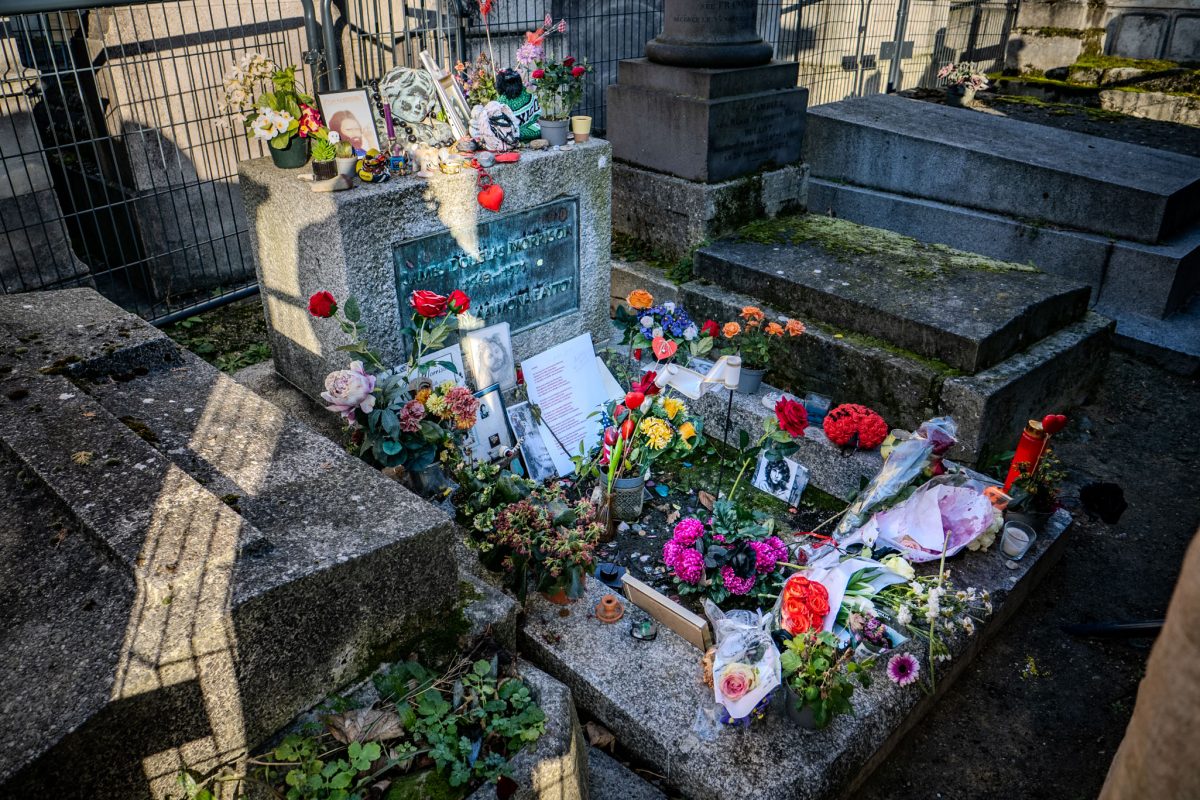 A wide shot of the stone grave of James Douglas Morrison surrounded by security fencing and covered in flowers.