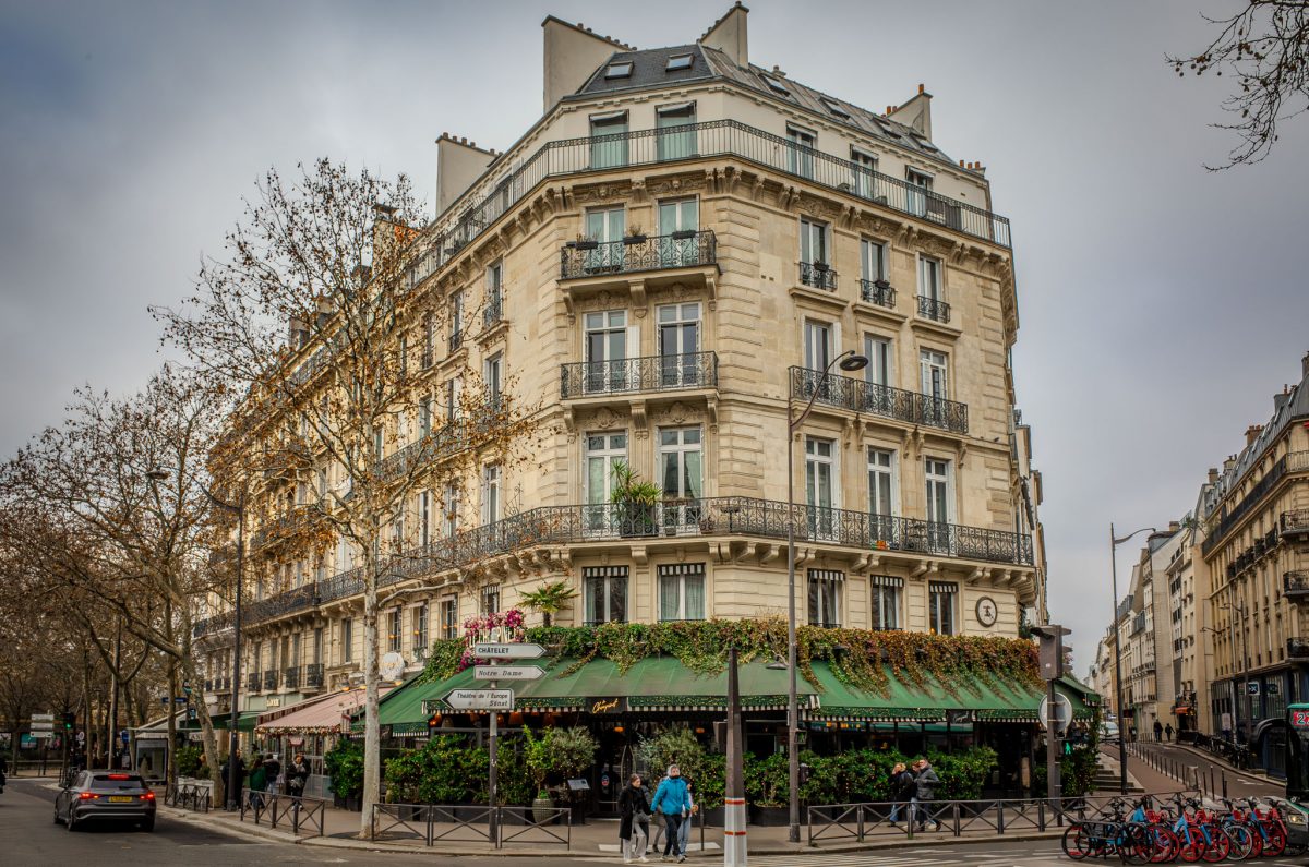 A classic Parisian Haussmann building on a street corner with a green-covered bistro on the ground floor.