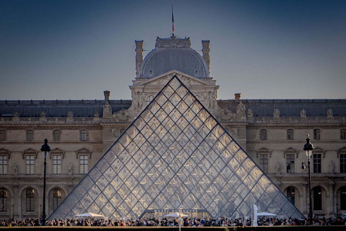 A symmetrical view of the Louvre glass pyramid in front of the historic palace at dusk.