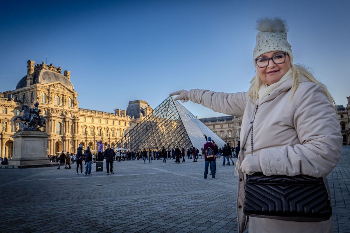 A woman in winter clothing pointing toward the Louvre Pyramid in Paris.