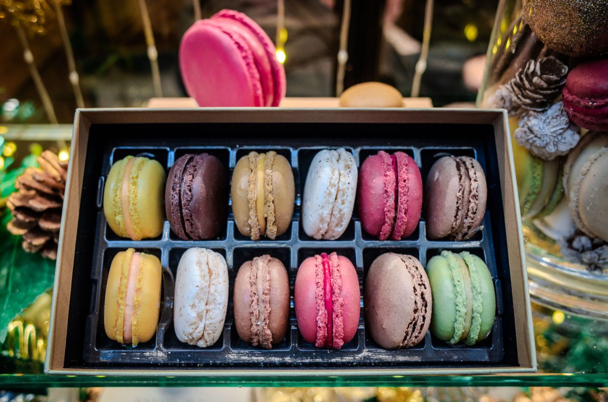 A box of colorful macarons including pistachio, chocolate, and strawberry flavors.