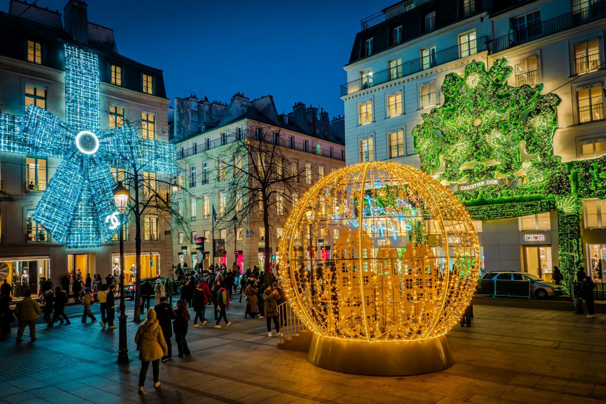 Brightly lit luxury store facades and a golden light orb on Rue Saint-Honoré in Paris.