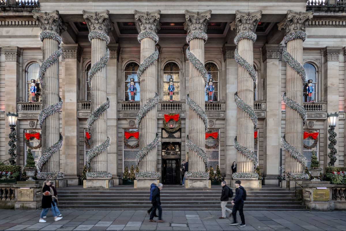 The grand exterior of The Dome in Edinburgh adorned with massive Christmas wreaths, red bows, and festive lights on its towering columns.