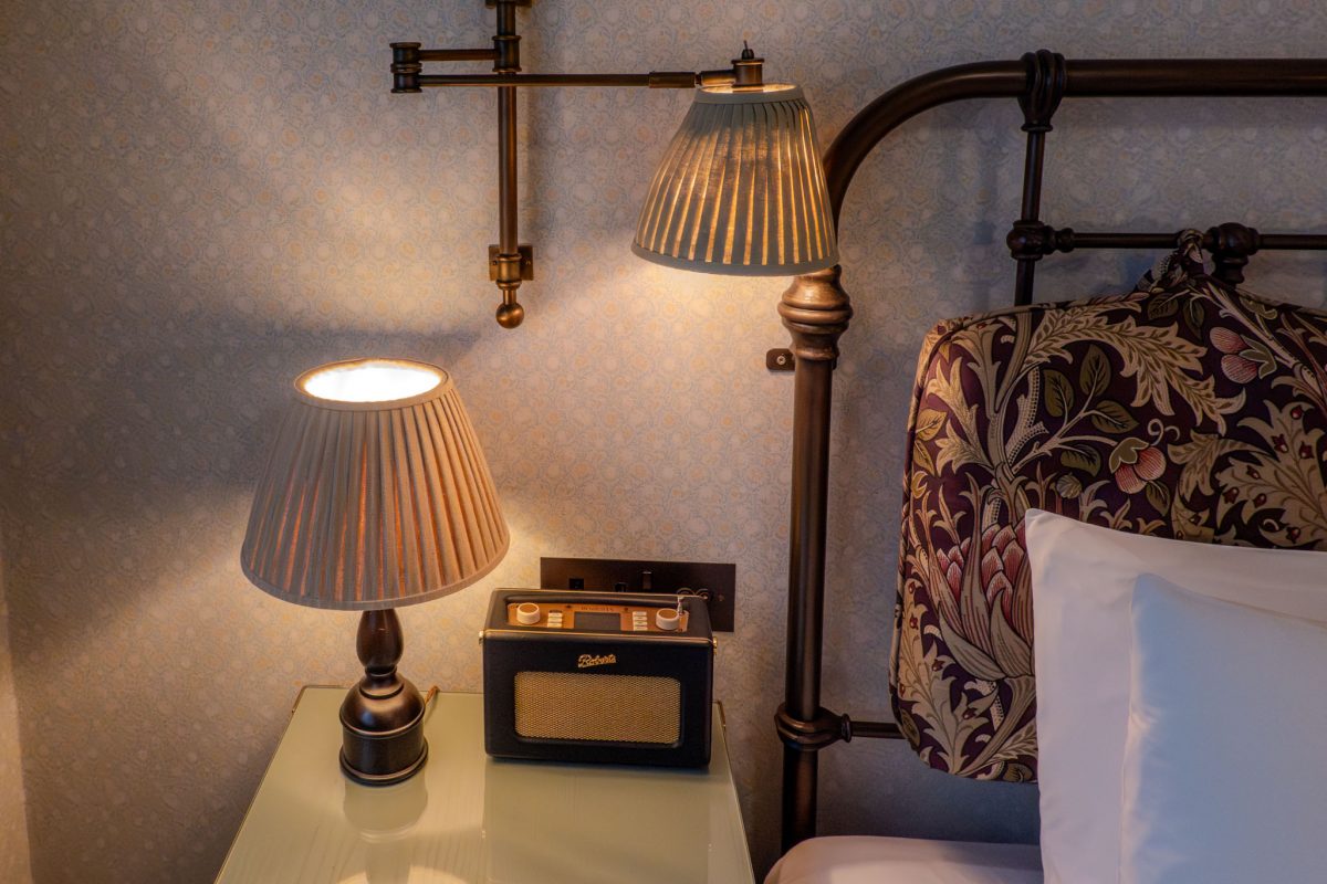 A pleated lampshade glowing next to a vintage Roberts radio on a glass table.