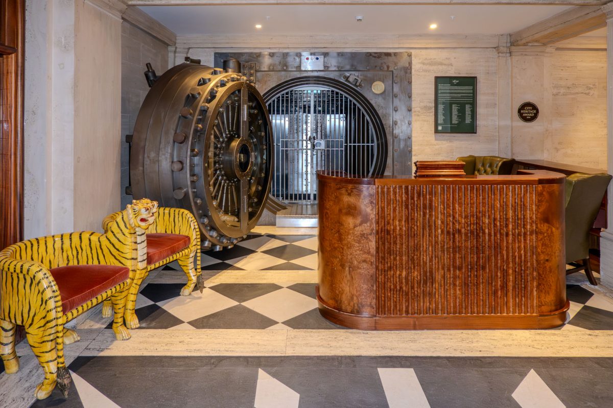 A massive circular vintage bank vault door next to a wooden reception desk and tiger-shaped benches.