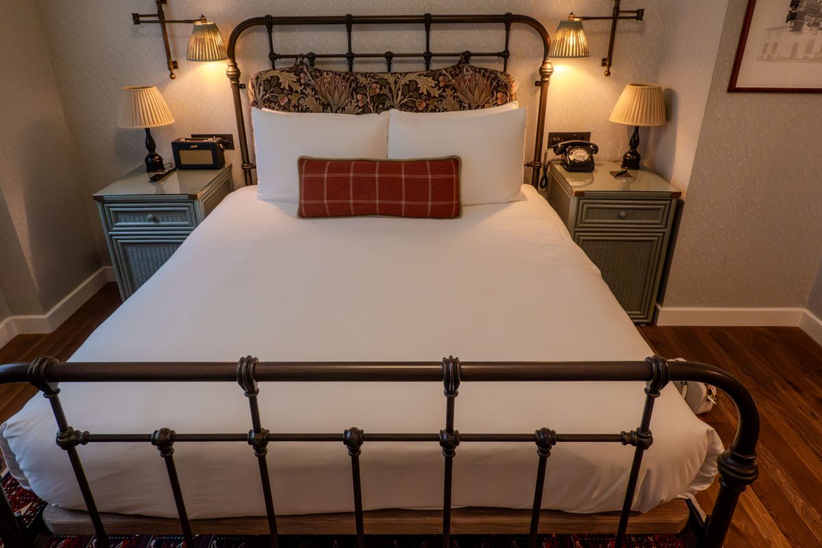 A luxury hotel bed with a wrought iron frame, floral headboard, and vintage bedside lamps.