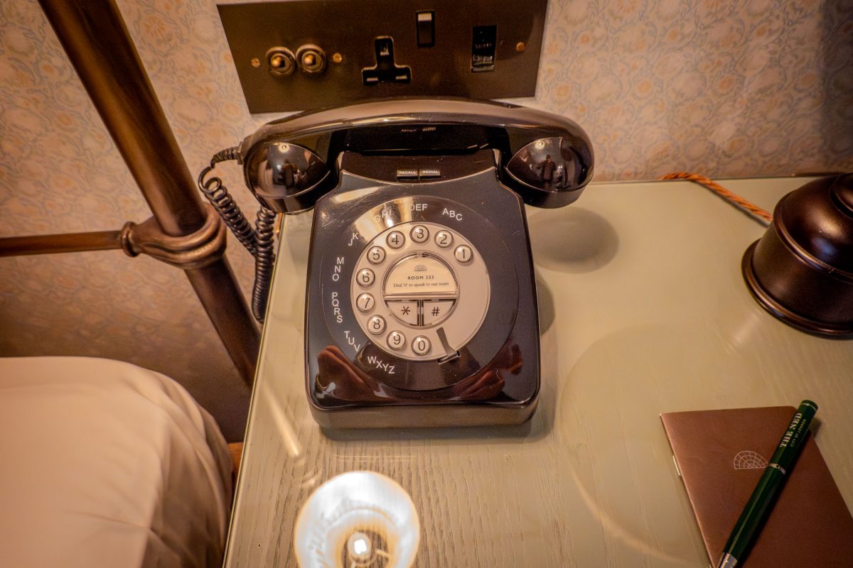 A black vintage-style rotary telephone sitting on a light-colored bedside table.
