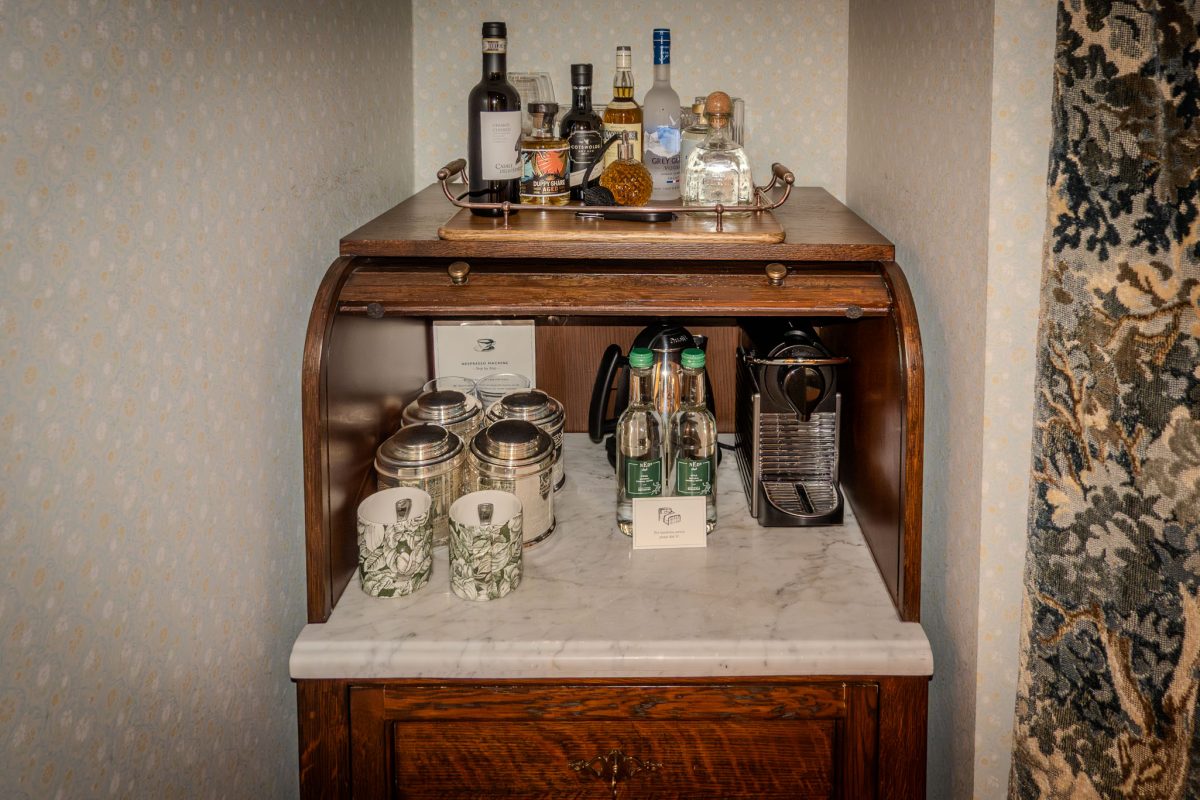 A wooden cabinet topped with spirits, crystal glassware, and a tea kettle.