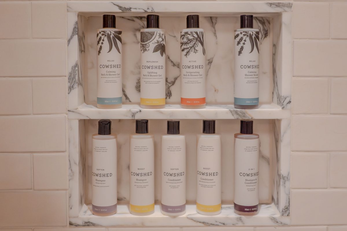 A variety of Cowshed bath and shower bottles neatly arranged on marble shelves.