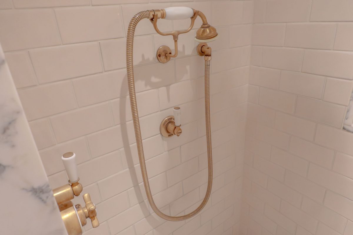 Ornate brass and porcelain shower controls on a white tiled wall.