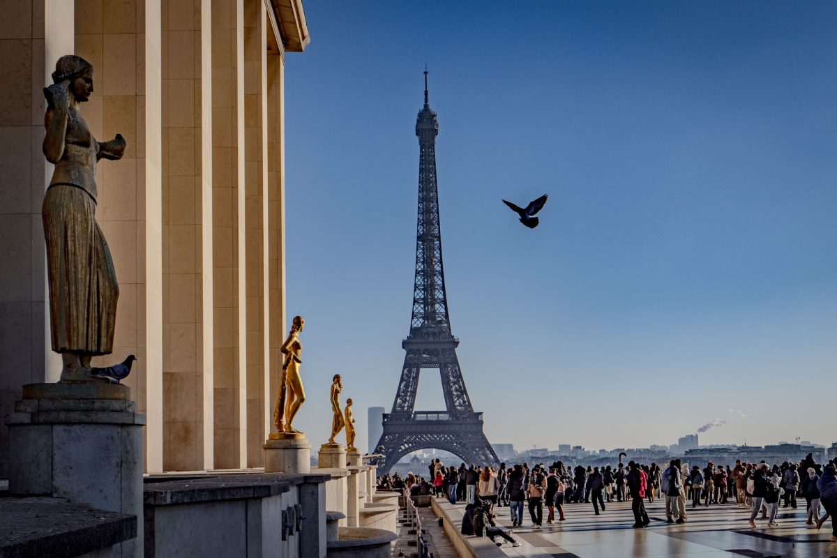 The Eiffel Tower centered between the statues and columns of the Trocadéro esplanade.