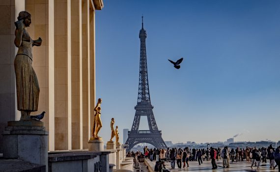 The Eiffel Tower centered between the statues and columns of the Trocadéro esplanade.
