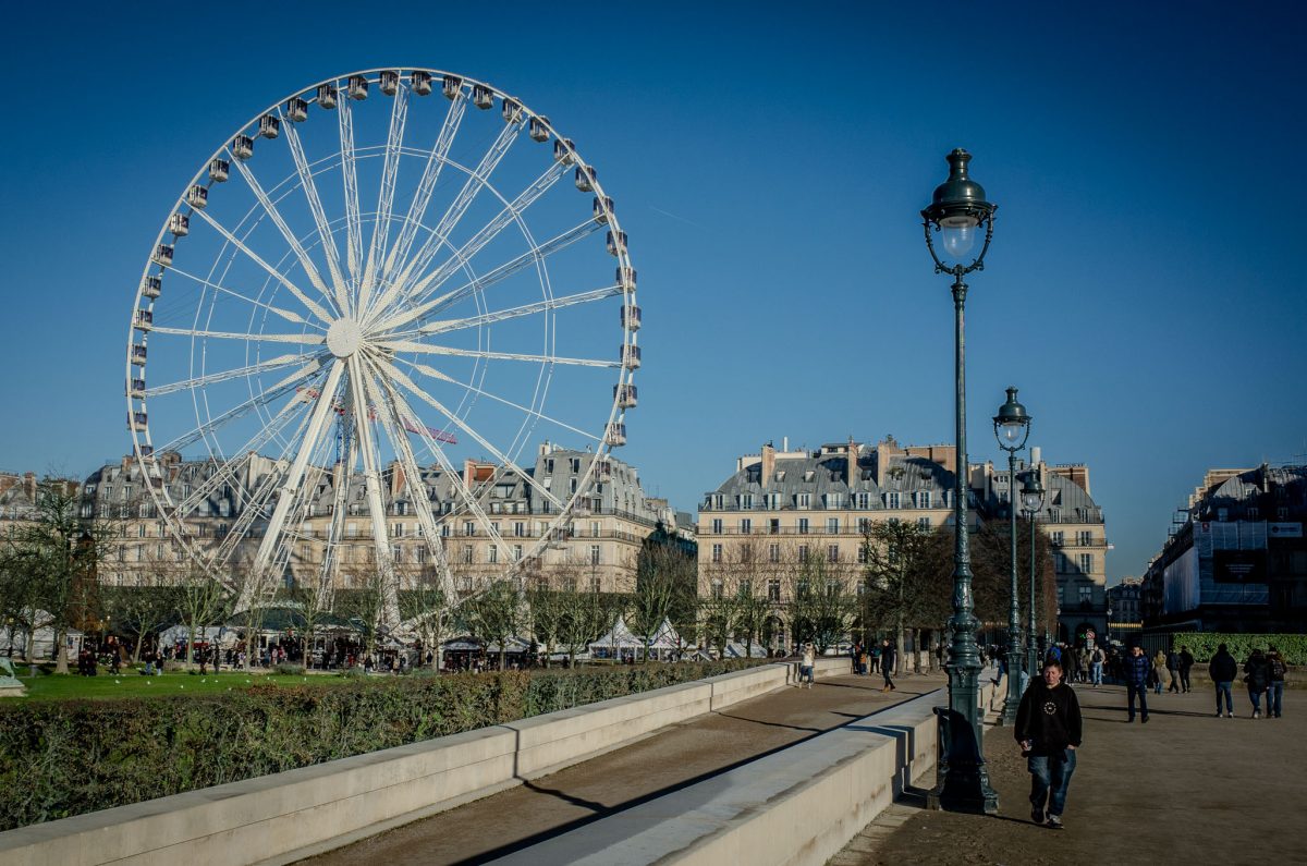Large white Ferris wheel in the Tuileries Garden during the Christmas market with Parisian buildings in the background.