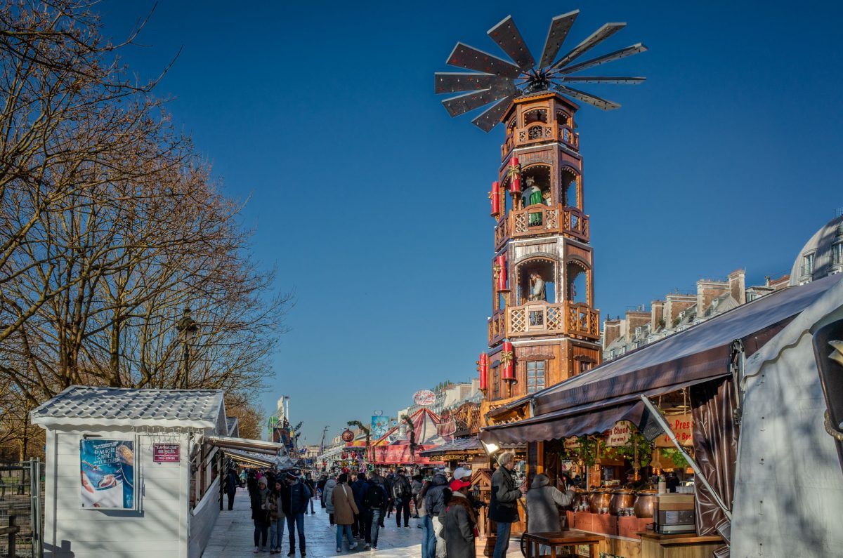 A tall wooden German-style Christmas pyramid at the Paris Tuileries Christmas market surrounded by crowds and food stalls.