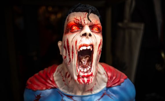 A close-up of a gruesome zombie-style superhero statue with glowing red eyes and a blood-stained face.